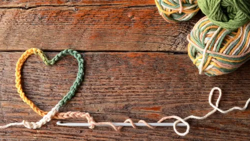 Yarn heart and needle on wooden surface.