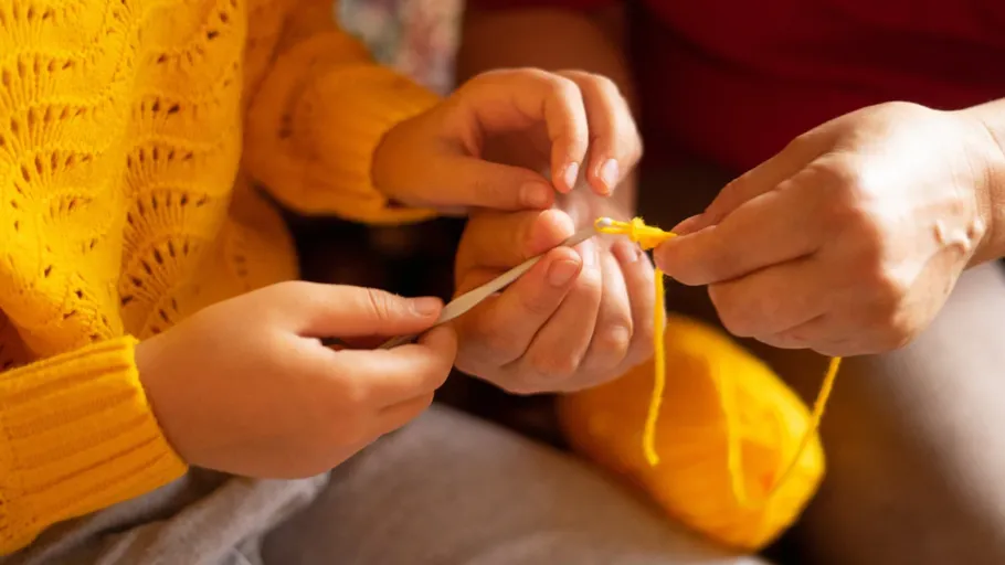 Hands crocheting with yellow yarn indoors.