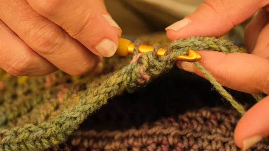 Hands crocheting with green yarn and hook.