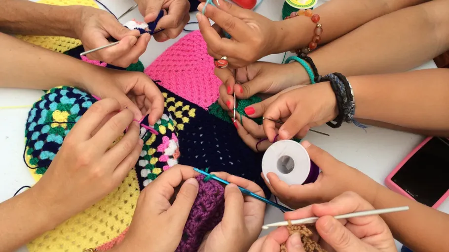Hands crocheting colorful yarn in group setting.