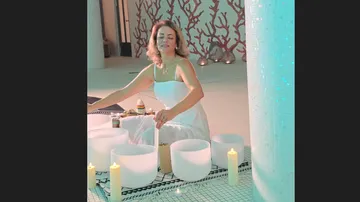 Woman playing sound bowls surrounded by candles.