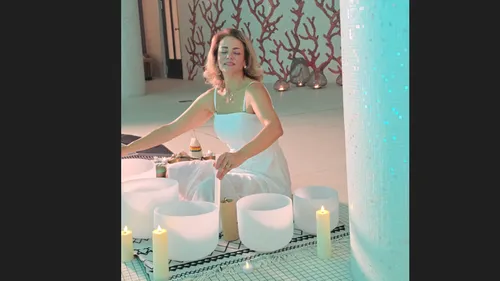 Woman playing sound bowls surrounded by candles.
