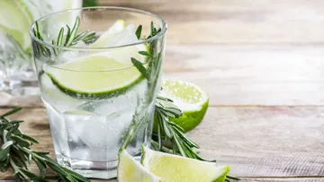 Glas mit Limette und Rosmarin auf Tisch.