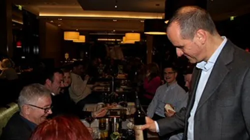 Man presenting wine to seated diners in restaurant.
