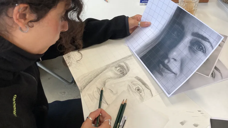 Person drawing a pencil portrait using a photo reference.