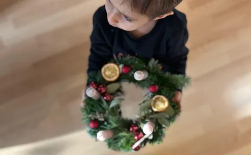 Child holding a decorated holiday wreath indoors.