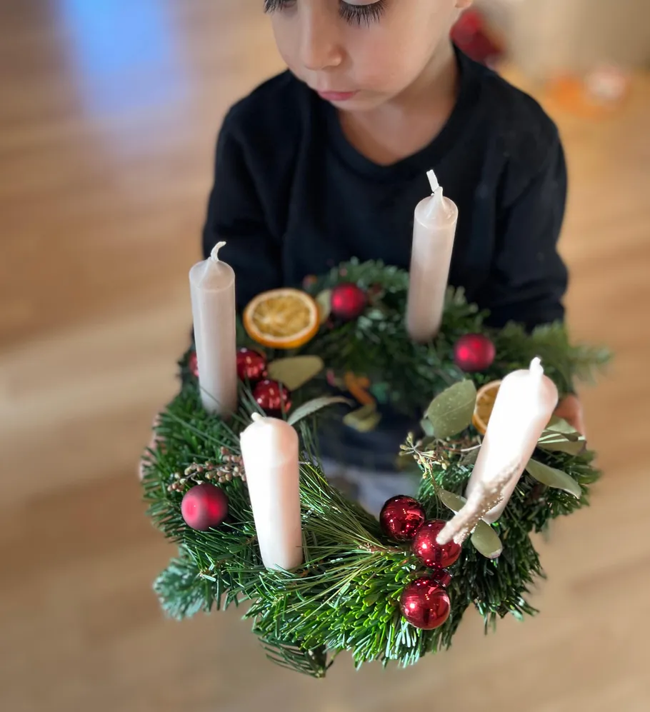 Child holding Advent wreath in room.