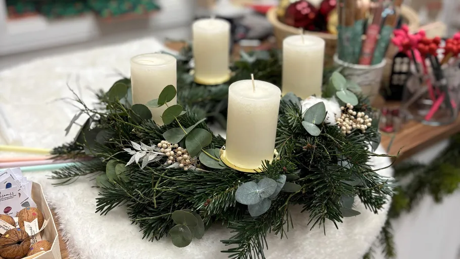 Four candles on decorative Christmas wreath indoors.