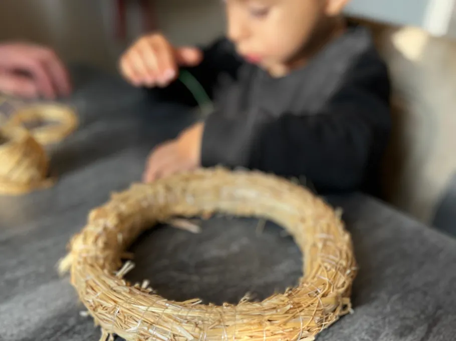 Child crafting wreath on table.