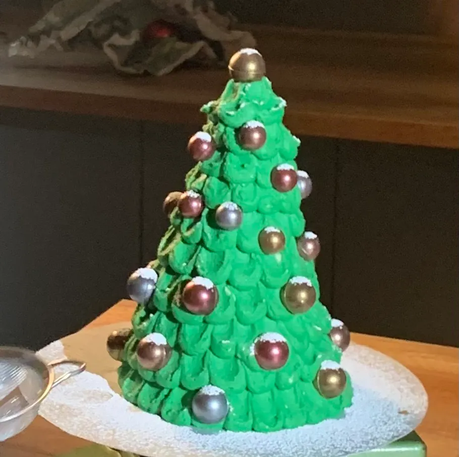 Grüner Weihnachtsbaumkuchen mit Dekorationen auf Tisch.