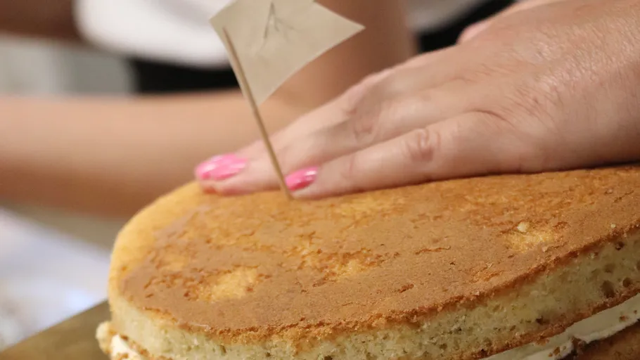 Hand drückt Kuchen mit rosa Nägeln.