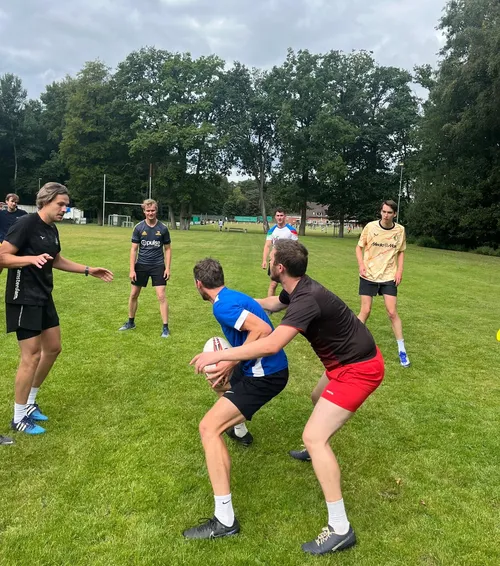 Group of men playing rugby on grass field.