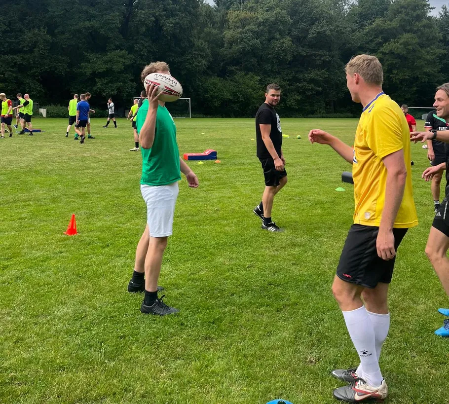 Gruppe spielt Rugby auf einem Rasenplatz.