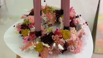 Blumenkranz mit rosa Kerzen auf Tisch.