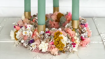 Bunter Blumenkranz mit grünen Kerzen drinnen.