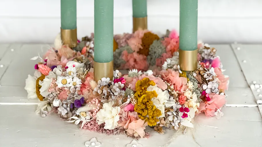 Colorful floral wreath with green candles indoors.