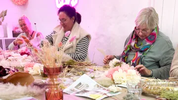 Frauen basteln Blumenarrangements am Tisch.