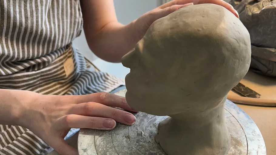 Person sculpts clay head on rotating platform.