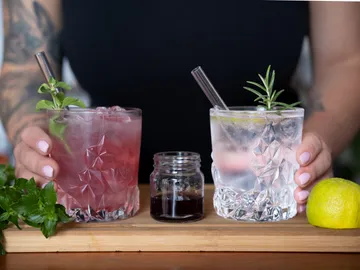 Two cocktails are held on a wooden board.