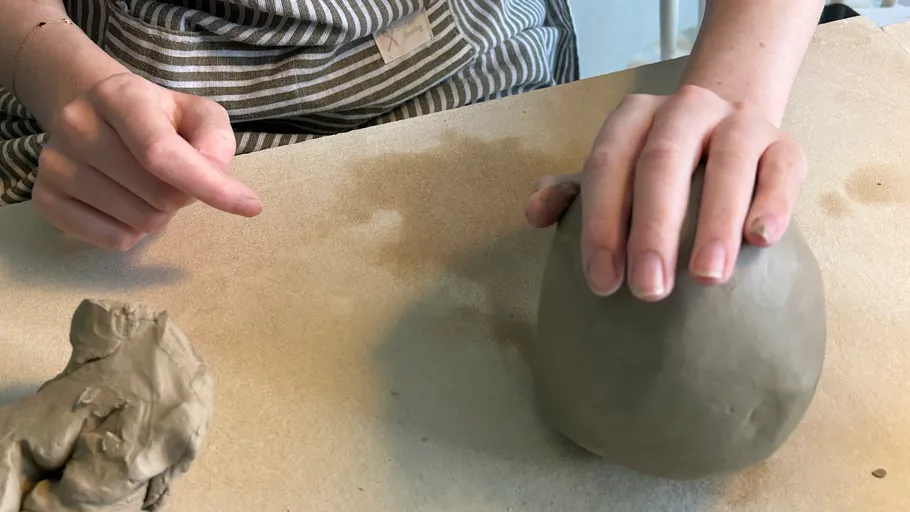 Person shaping clay ball on tabletop.