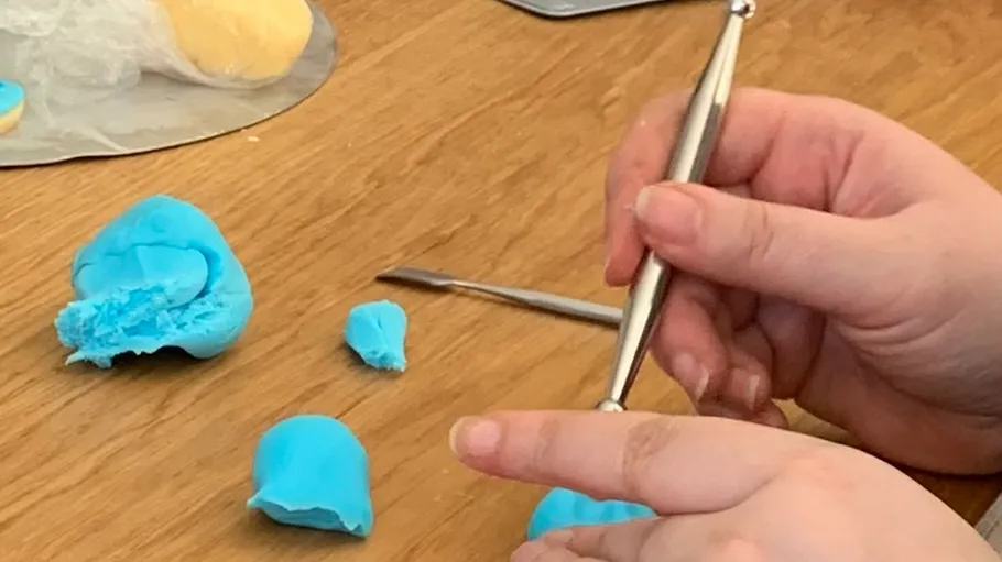 Hands sculpting blue clay on wooden table.