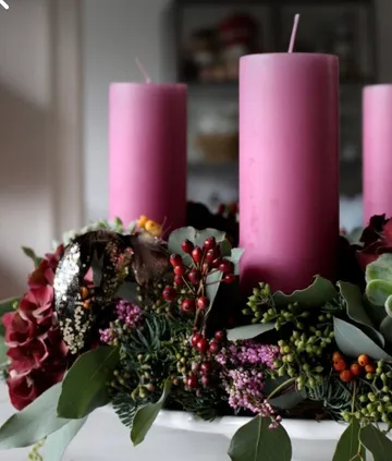 Drei lila Kerzen mit Blumenkranz.