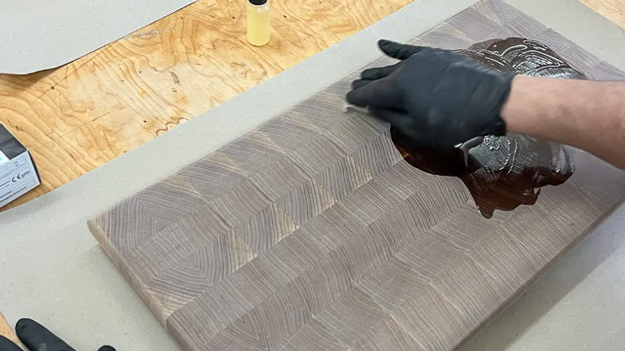 Behandschuhte Hand trägt Öl auf Holzbrett auf.