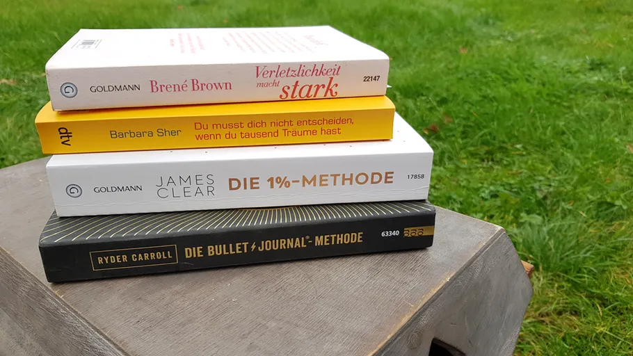 Stack of books on a wooden table outdoors.