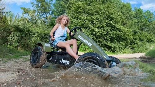 Child driving go-kart splashing through mud.