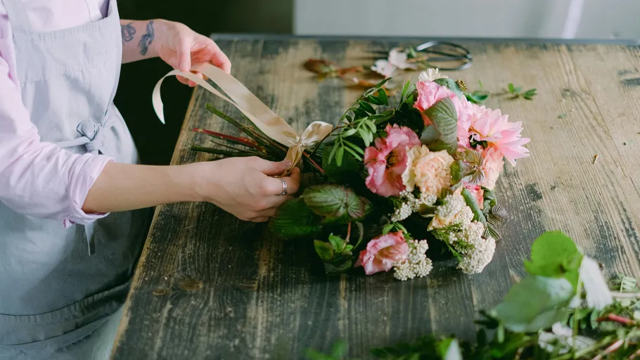 Person ties ribbon on a flower bouquet.