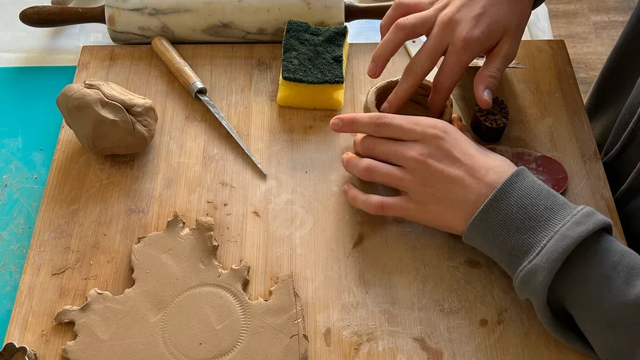 Person shaping clay on wooden board.