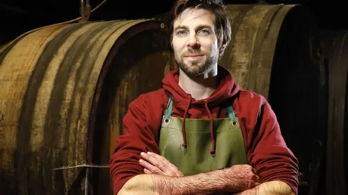 Man in apron standing by large barrels.