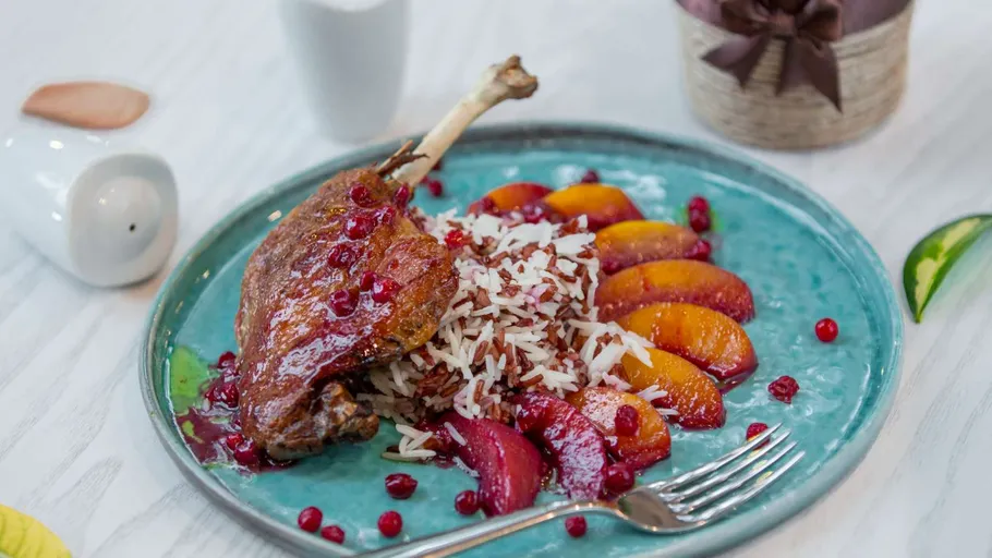 Duck leg with rice, fruit garnished on plate.