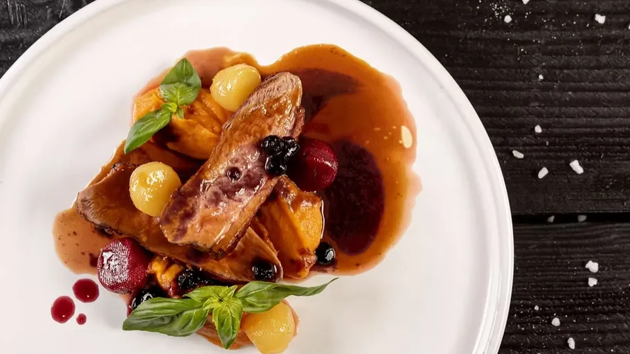 Gourmet dish with meat, fruit, sauce, basil garnish.