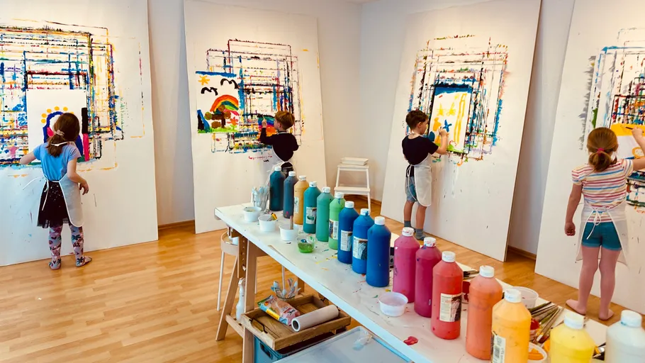 Children painting on large canvases indoors.