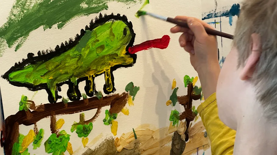 Person painting a green creature on canvas.