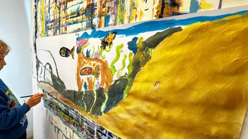 Child painting colorful artwork on large canvas.