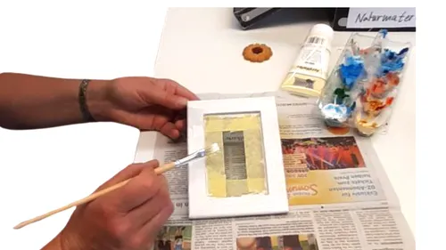 Person painting small canvas on newspaper.