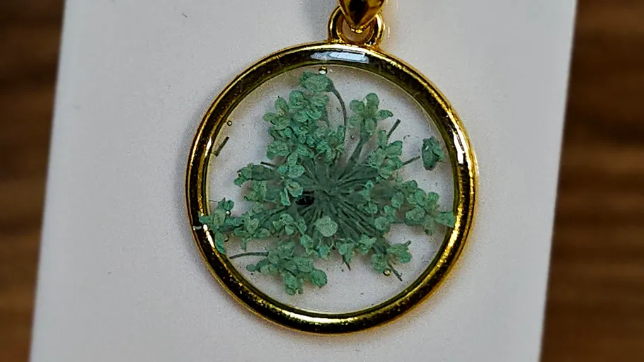 Gold pendant with pressed green flower inside.