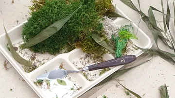 Moos, Blätter und Malspachtel auf Tablett.