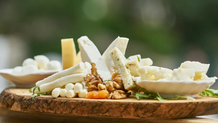 Cheese and nuts on wooden platter outdoors.