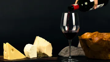 Red wine poured into glass near assorted cheeses.