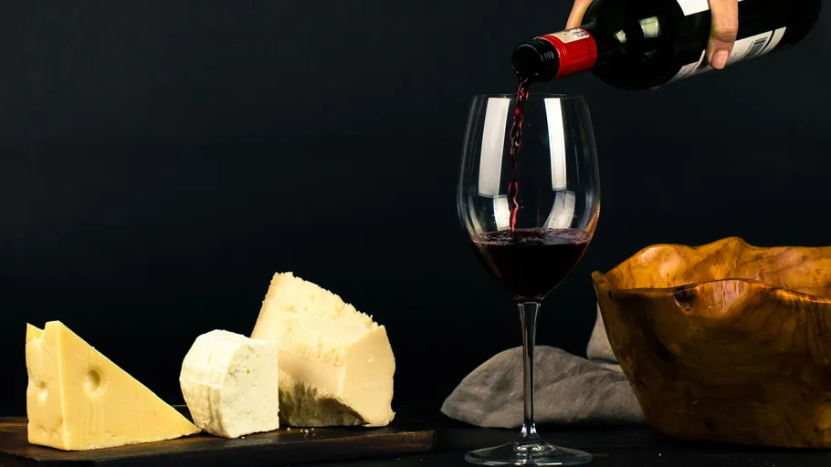 Red wine poured into glass near assorted cheeses.