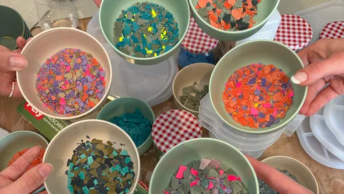 Hands holding bowls of colorful plastic pieces.