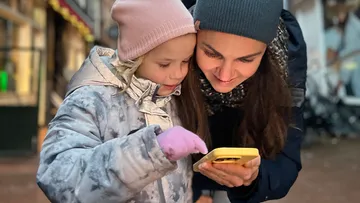 Kind und Erwachsener schauen auf Handy draußen.
