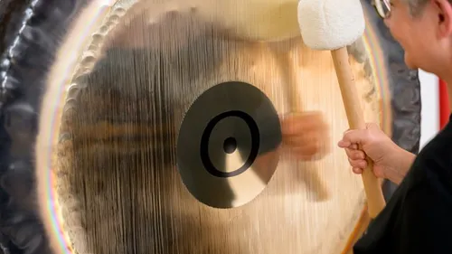 Person striking large gong indoor setting.