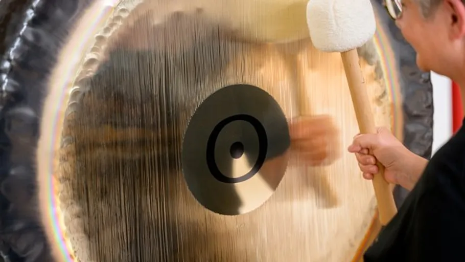 Person schlägt großen Gong in Innenraum.