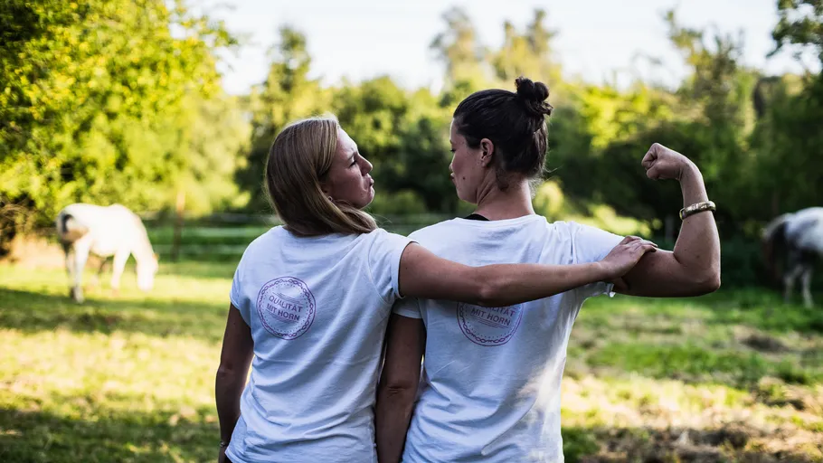 Two women flexing arms in a field.