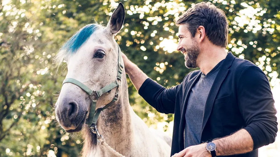 Man petting horse outdoors among trees.