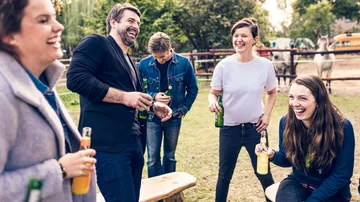 Gruppe von Freunden lacht draußen mit Getränken.